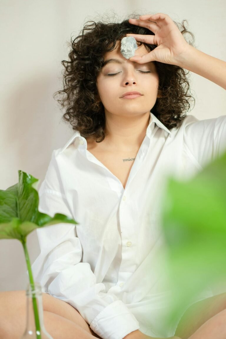 Curly-haired woman meditating with a crystal on her forehead, indoors.