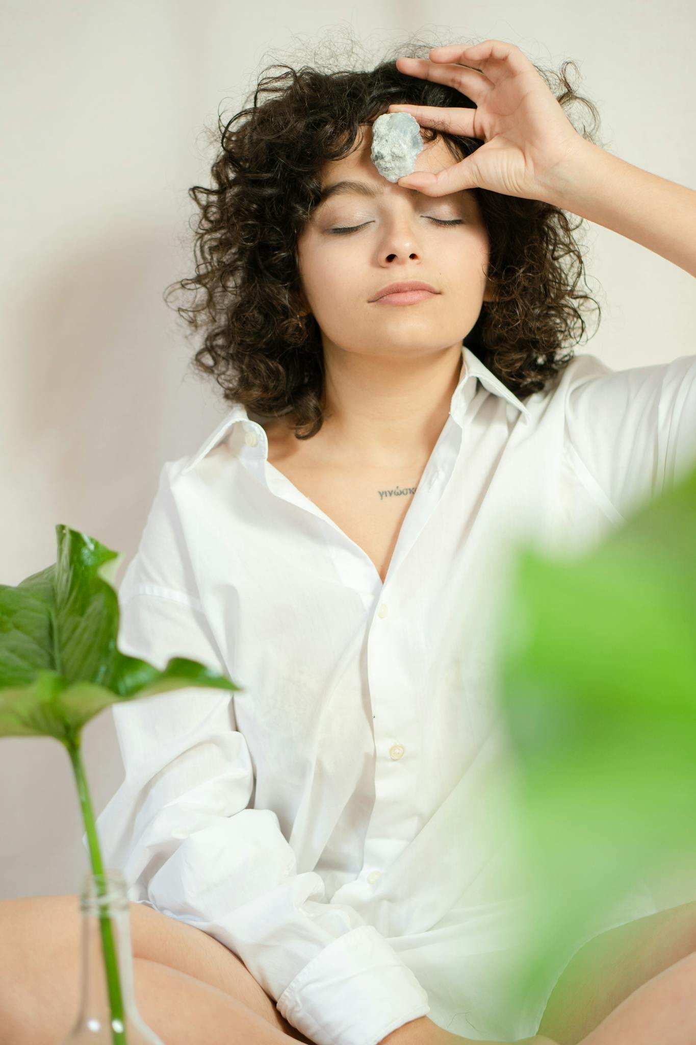 Curly-haired woman meditating with a crystal on her forehead, indoors.
